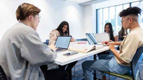 Students working around a table with laptops open.